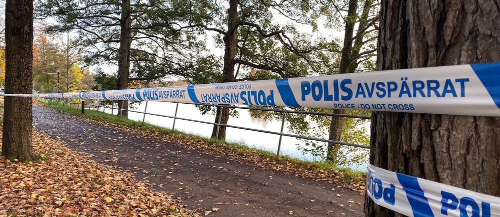 Avspärrad väg vid en sjö. Blått polisavspärrningsband sträcker sig längs med vägen.