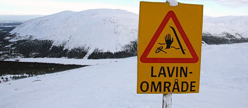 Skylt vid snötäckt berg varnar för lavinområde.