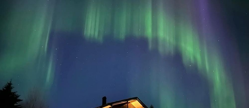 Ett stort norrsken som syns bakom en stuga i Åre.
