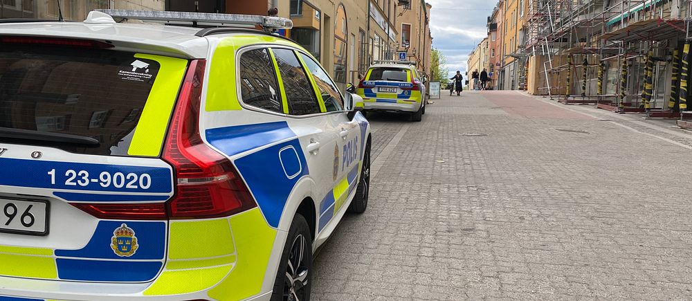 Två polisbilar parkerade längs en tom gata mellan hus i stadsmiljö.