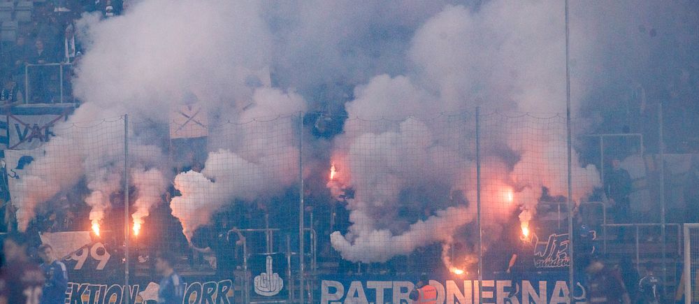 Fotbollsfans bränner pyroteknik och skapar tätt rökmoln i publikhavet.