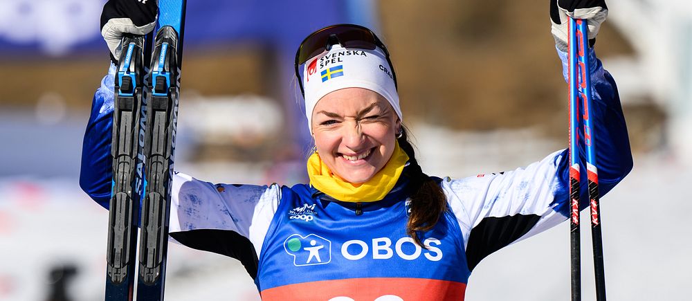 Skidåkare med startnummer 36 höjer båda stavarna vid målgång i tävling.