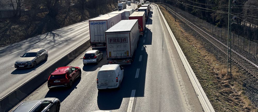 Trafikstockning på motorväg vid sidan av järnvägsspår, kvarstående vinterträd.