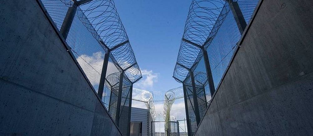Fängelsemurar i betong med stängsel och taggtråd.