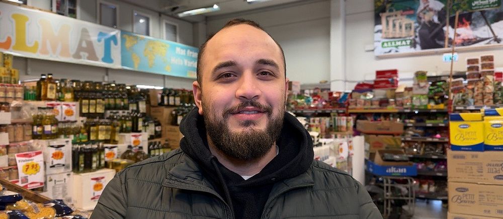 Man i grön jacka står framför hyllor i en matbutik.