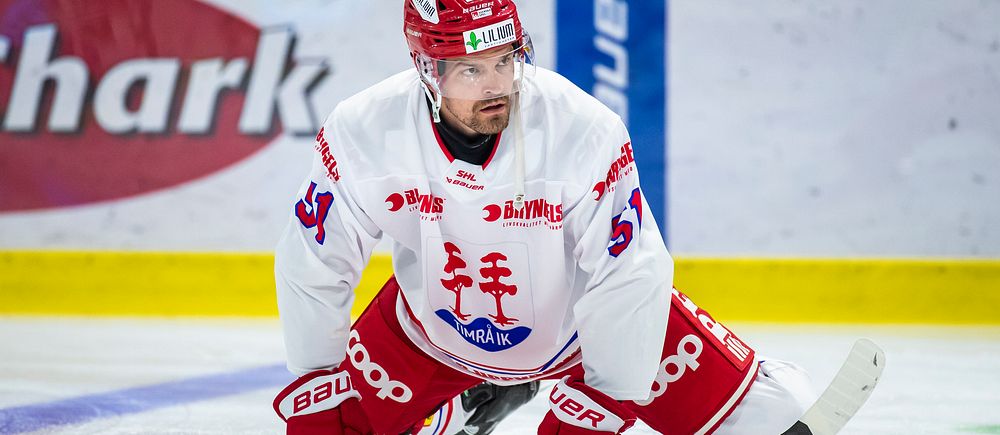 Hockeyspelare i vit och röd dräkt stretchar på isen.