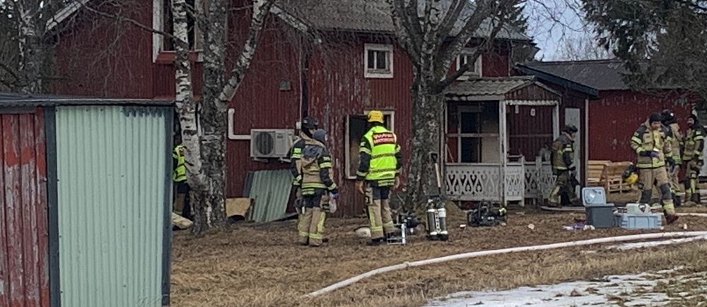 Brandmän undersöker rött hus med utrustning. Spår av snö på marken.