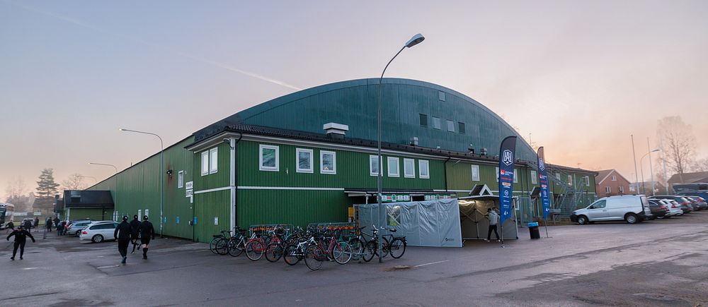 Grönt sportkomplex vid solnedgång. Cyklister och gående passerar på vägen.