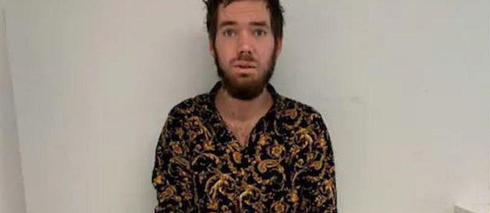 Person med mörkt, mönstrat skjorta står mot en vit vägg.