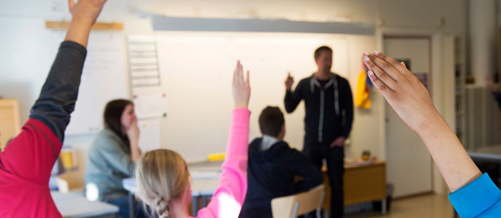 Elever räcker upp handen i ett klassrum.