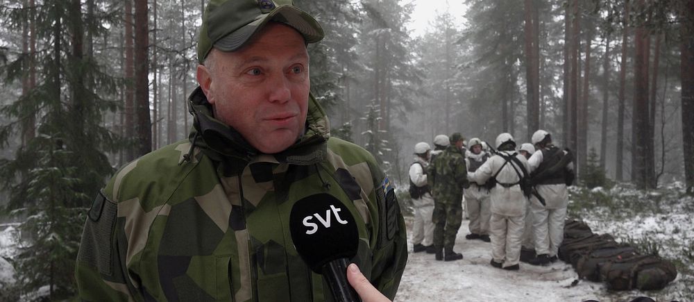 Reporter intervjuar soldat i vinterkamouflage i skogsmiljö, fler soldater i bakgrunden.