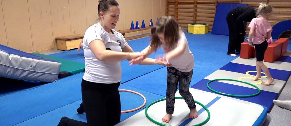 Kvinna i gympasal instruerar barn som ska göra ett hopp eller volt.
