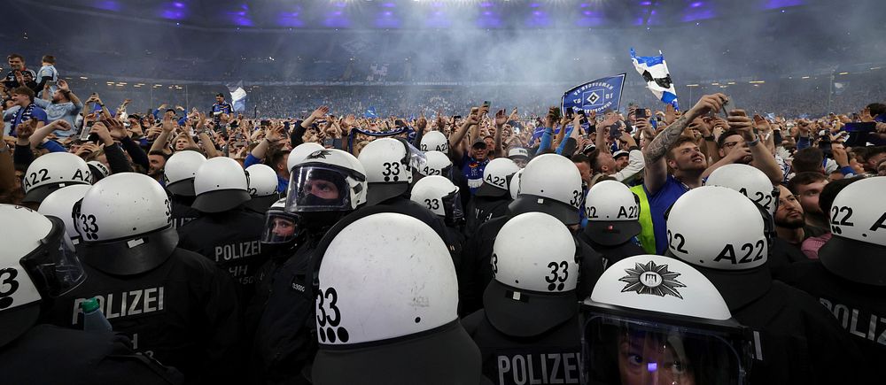 Poliser i hjälmar bildar kedja framför stor fotbollspublik på en upplyst arena.