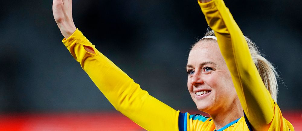 Svensk fotbollsspelare i gul tröja sträcker upp händerna i luften.