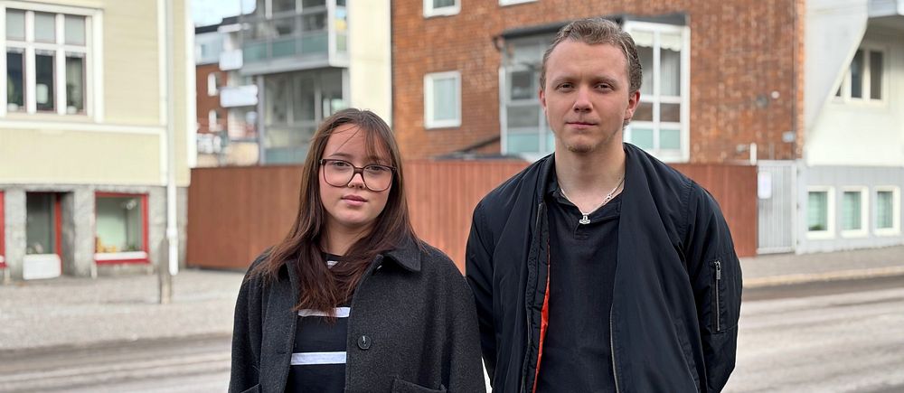 Ebba Eklund och Gustav Persson står utomhus framför en rad av byggnader.