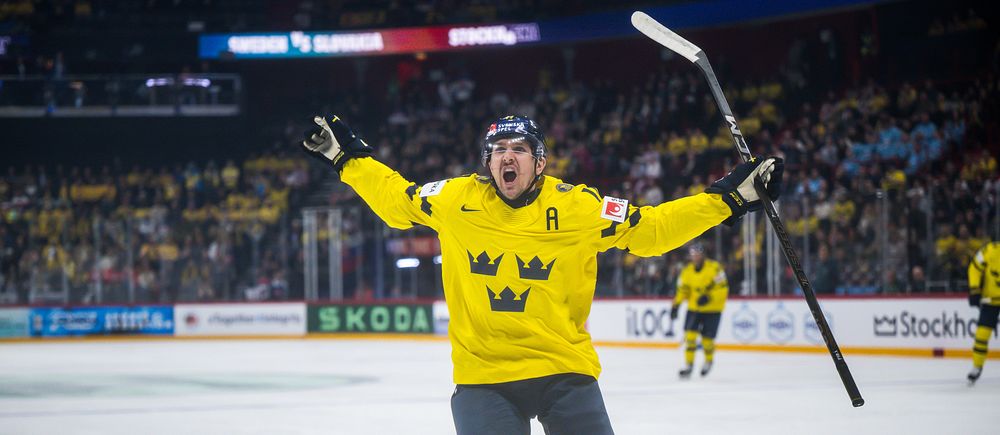 Svensk ishockeyspelare jublar efter mål under match, publik syns i bakgrunden.