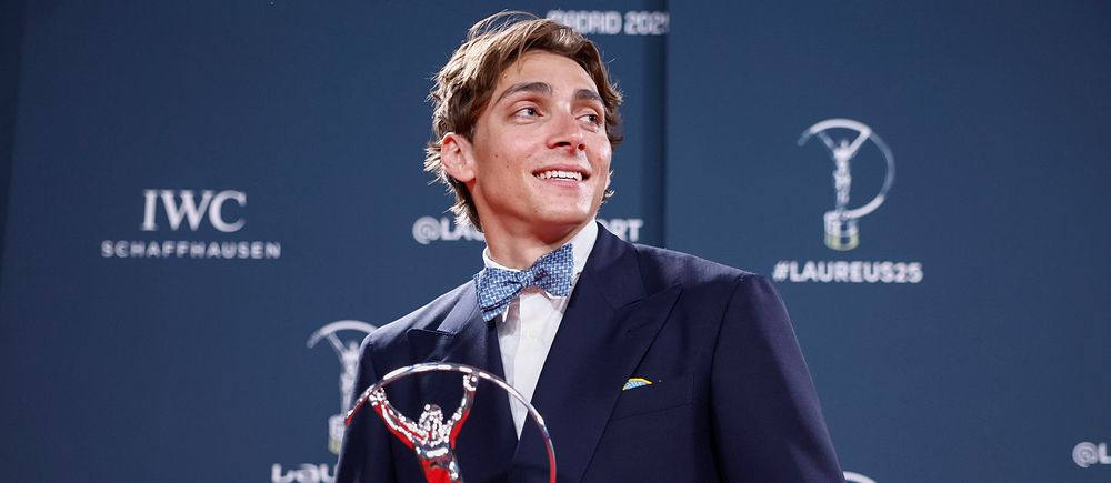 Man i kostym håller Laureus-utmärkelse framför sponsorskärmar.