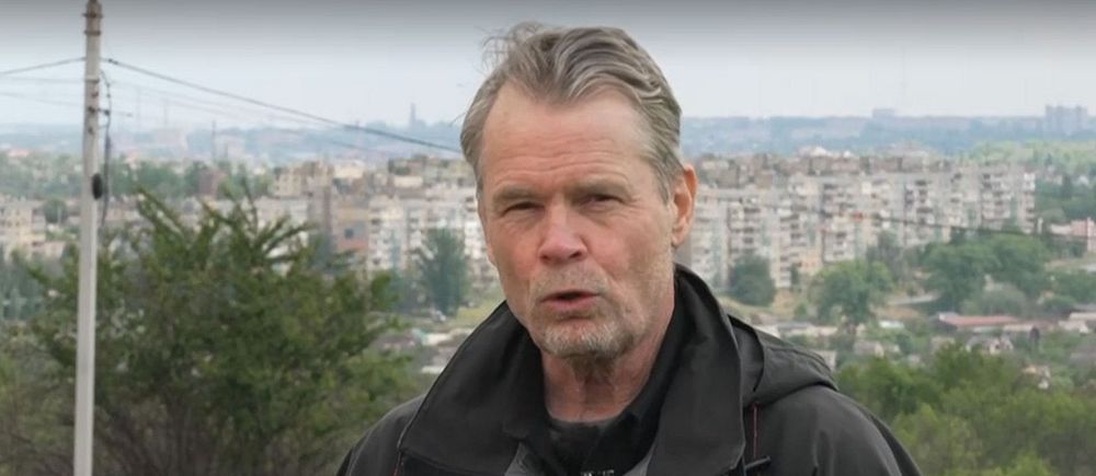 Person utomhus med stad och parkerade bilar i bakgrunden.