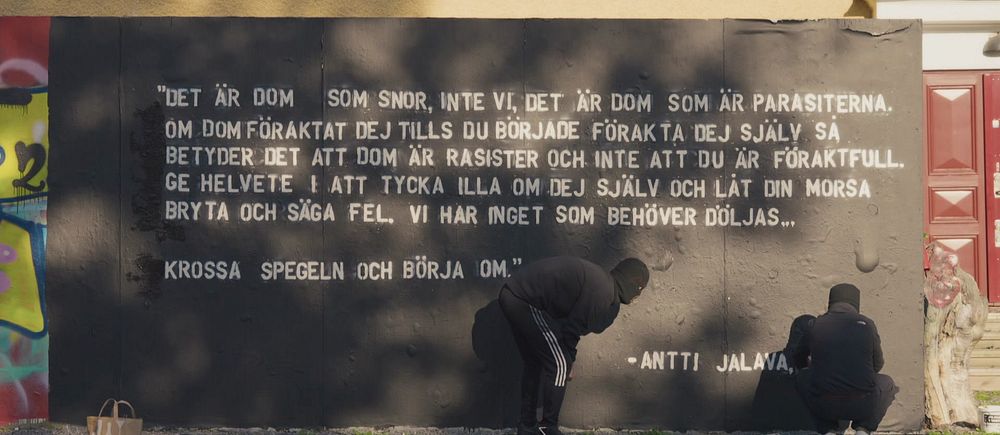 två graffitikonstnärer färdigställer ett citat på väggen