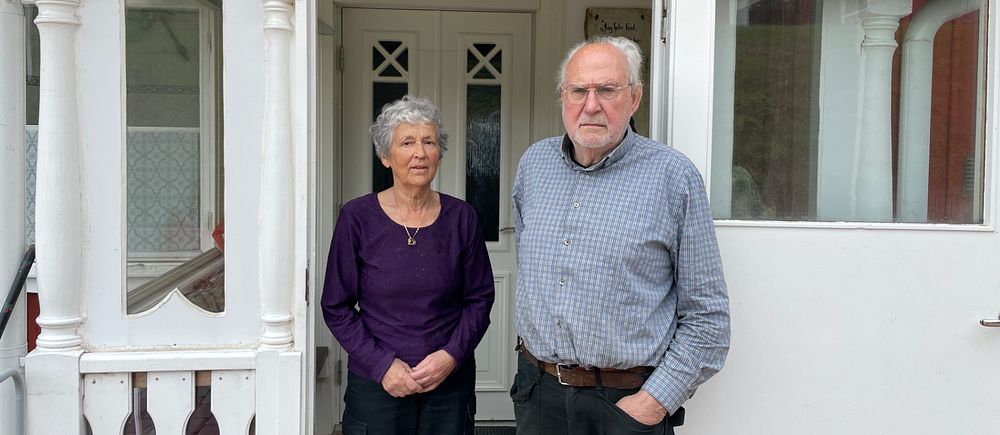 En kvinna och en man står utanför en vit verandadörr, kvinnan i lila tröja, mannen i blå skjorta.