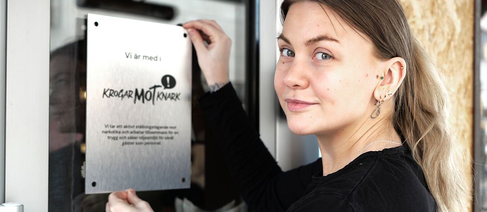 En person sätter upp en metallskylt med text på en glasdörr.