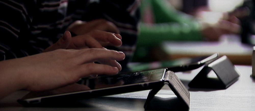Personer som använder surfplattor i ett klassrum. Fokus på händer och skärmar.