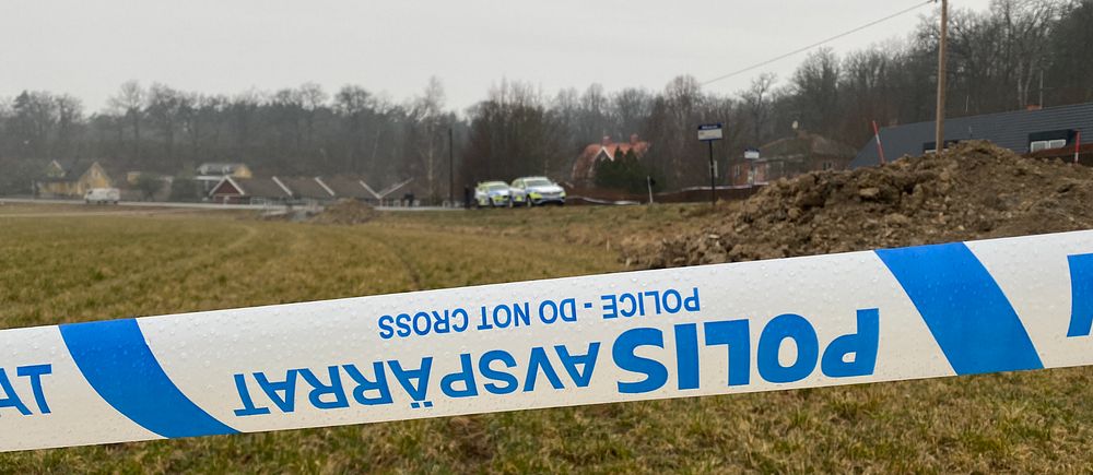 Polisavspärrning vid ett trädfyllt område på en gräsmatta utanför en stad.