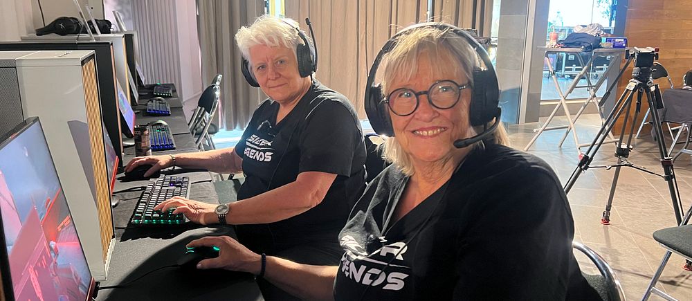 Två personer sitter vid varsin dator med headset och spelar datorspel i en studio.
