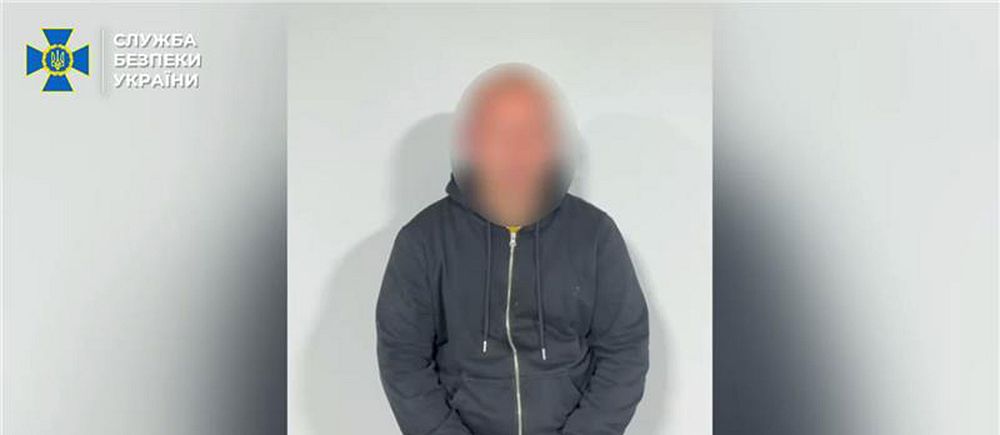 En man med blurrat ansikte sitter på en stol med knäppta händer framför en vit vägg. Bilden kommer från Ukrainska SBU via Telegram.