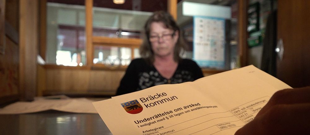 Mona Wannberg sitter med glasögon framför ett skrivbord. I förgrunden sen man ett dokument där det står att hon blivit avskedad från sin tjänst i Bräcke kommun.