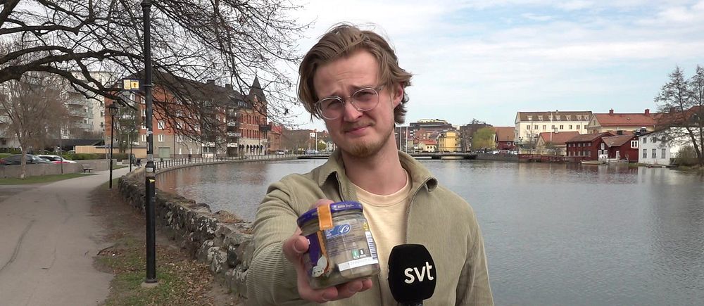 Reporter håller mikrofon och sillburk vid Eskilstunaån.