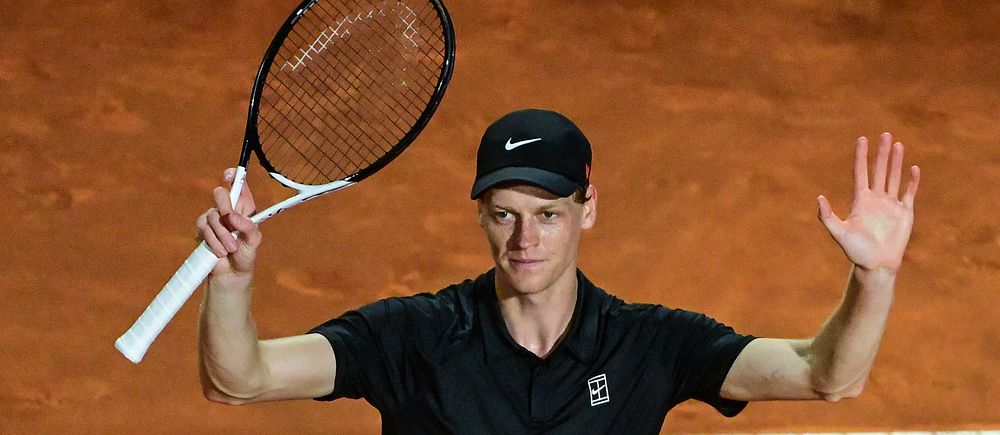 Tennisspelare i svart kläder lyfter armarna på en grusplan efter en poäng.