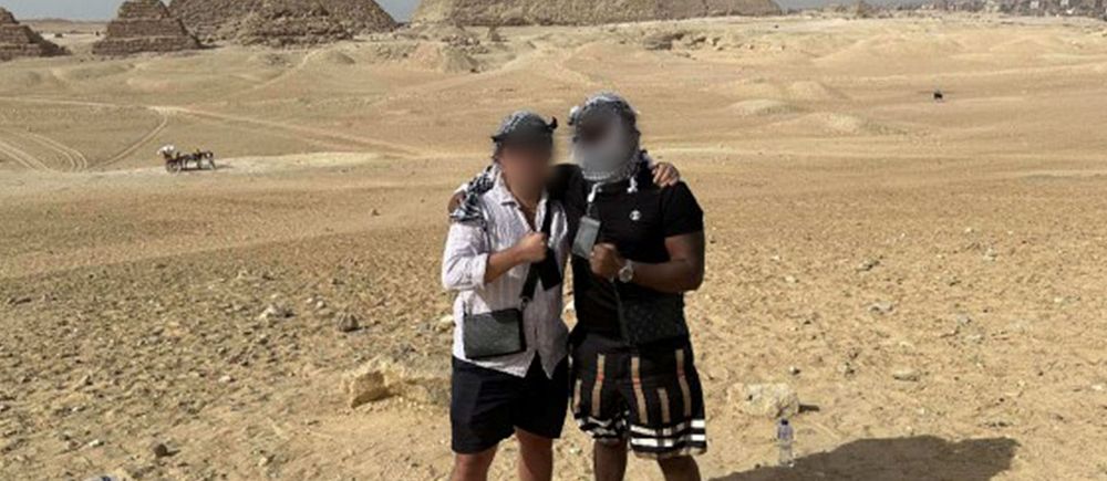 Två personer står tillsammans i öknen med pyramider i bakgrunden.