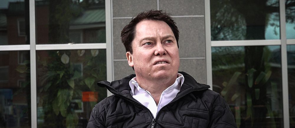 Daniel Svedin, ordförande för Dalarnas läkarförening sitter utomhus framför en glasvägg vid lasarettet i Falun iklädd svart jacka och vit skjorta.