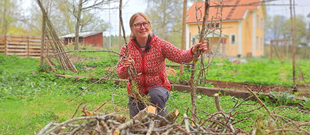 Hanna Pohjola står med kvistar och grenar i hand bakom en rishög framför sitt hus.