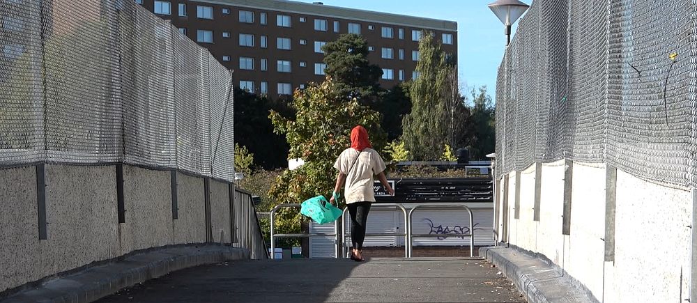 en flicka i hijab går på en bro, i bakgrunden ett höghus