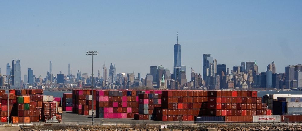 Manhattans skyline syns bakom höga staplar med fraktcontainrar.