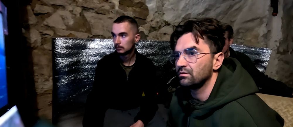 Två personer sitter framför drönar-skärmar i ett rum med stenmur och isolering.