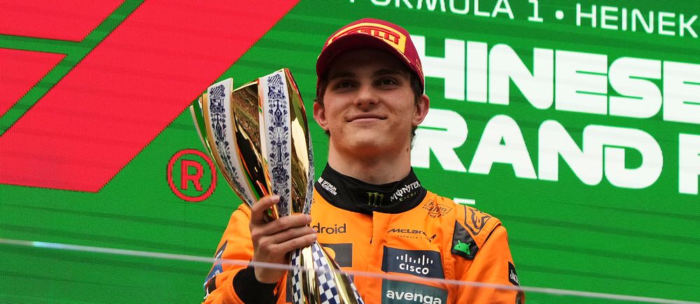 Formel 1-förare i orange overall håller upp en pokal vid prisceremoni.