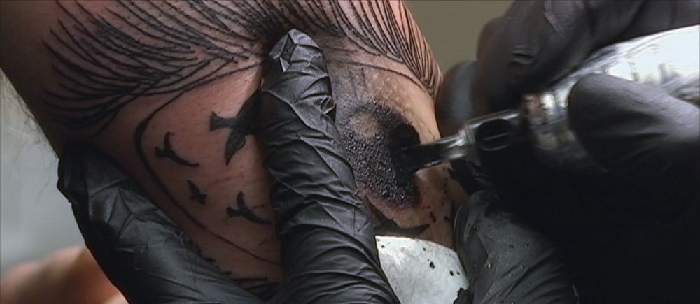 Hand med svart handske som tatuerar en arm