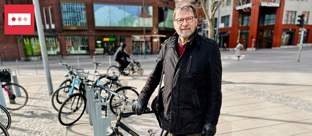 Man i svart jacka står vid cykelställ i stadsmiljö. Flera cyklar parkerade runt omkring.