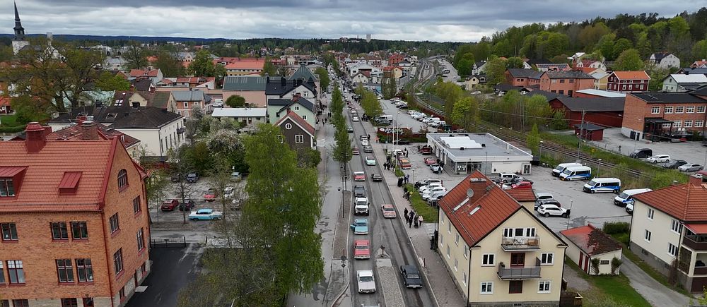 Lång bilkö genom tätort, omgiven av bostadshus och bilar under molnig himmel.