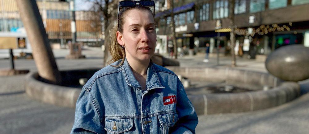 Judi Manaj i jeansjacka står vid tomt torg i Skellefteå med fontän och stadshus i bakgrunden.