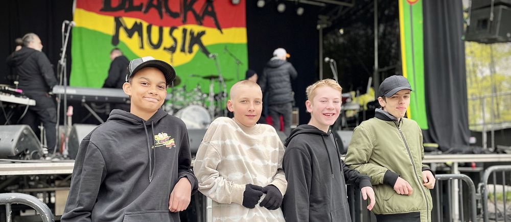 Fyra ungdomar framför en scen med banderoll där det står ”Beacka Musik”, scenfolk i bakgrunden.