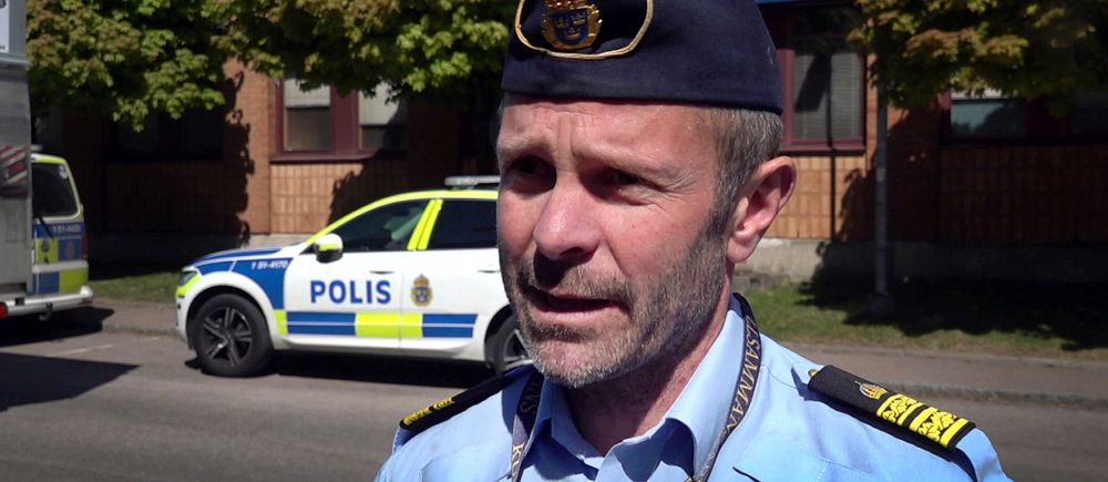 En polis ger intervju utomhus med polisbil i bakgrunden och SVT:s mikrofon synlig.