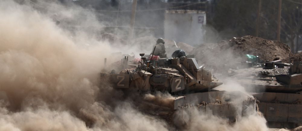 Israelisk stridsvagn vid Gazas gräns omgiven av damm och rök.