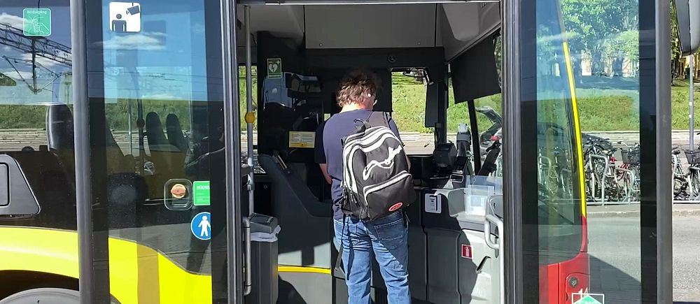 Person med ryggsäck kliver på en stadsbuss genom framdörren och visar biljett.