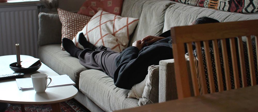 Kvinna vilar på en soffa i ett vardagsrum med kuddar och ett soffbord – och berättar om hur hon lever med konstant smärta efter en operation mot inkontinens som kallas TVT-O.