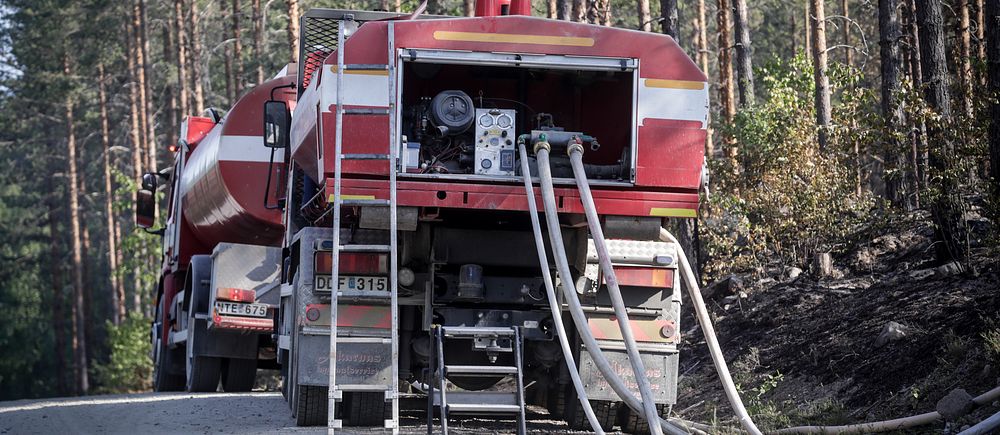 Tankbil med slangar parkerad på grusväg omgiven av tallskog.