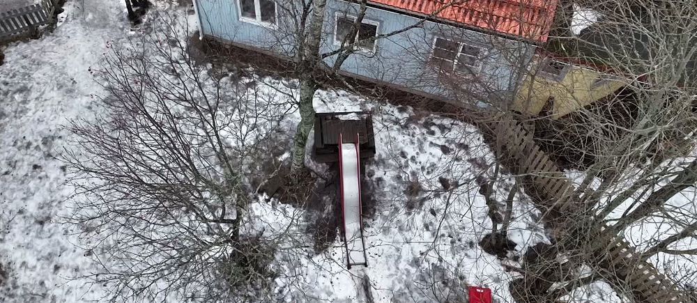Snötäckt trädgård med rutschkana och ett blått hus med tegeltak i bakgrunden.